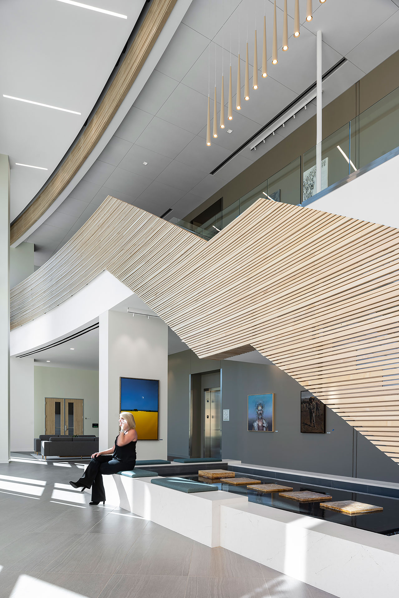 Interior at Ionis Conference Center lobby with view of water feature beneath the staircase and woman sitting at edge