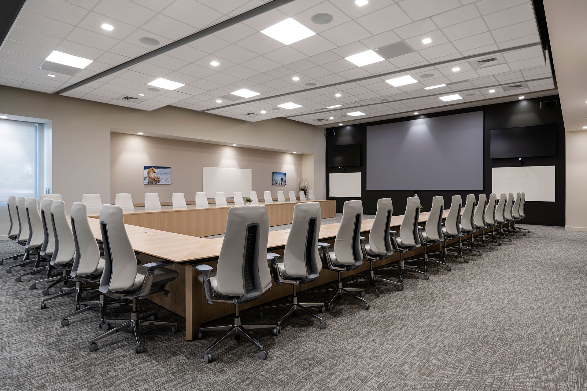 Interior at Ionis Conference Center conference room with U-shaped table, chairs, and several screens