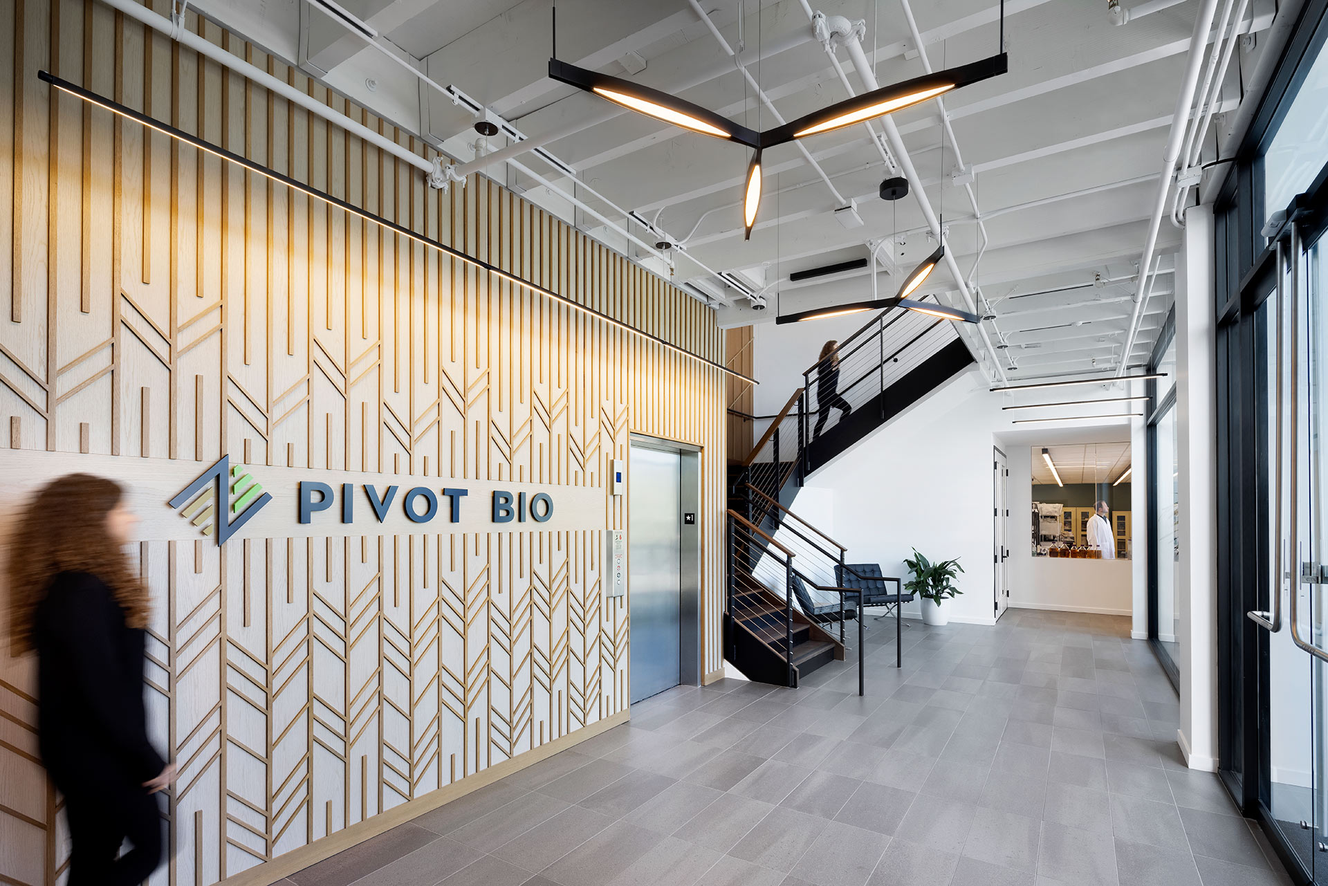 Interior at Pivot Bio life science facility, lobby with wood slat design feature, elevator, stairway, and view into lab