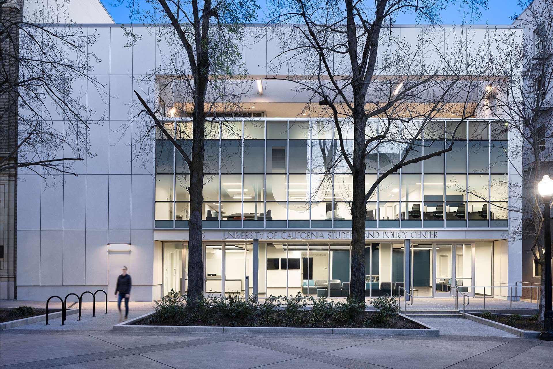 Exterior at UC Center Sacramento academic facility, evening view of the front of the building with UC signage and someone walking outside