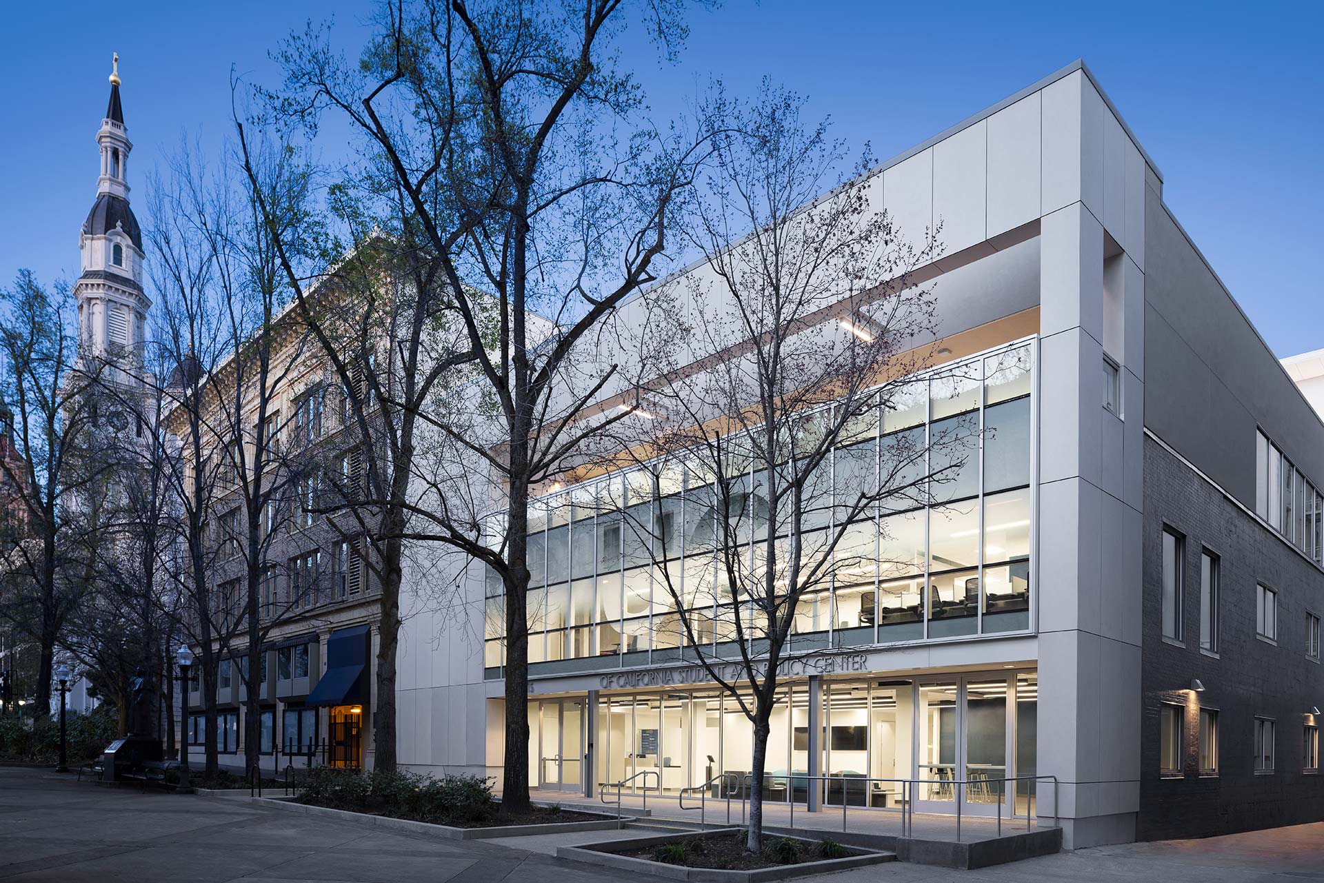 Exterior at UC Center Sacramento academic facility, evening view of the front of the building with UC signage and adjacent city buildings