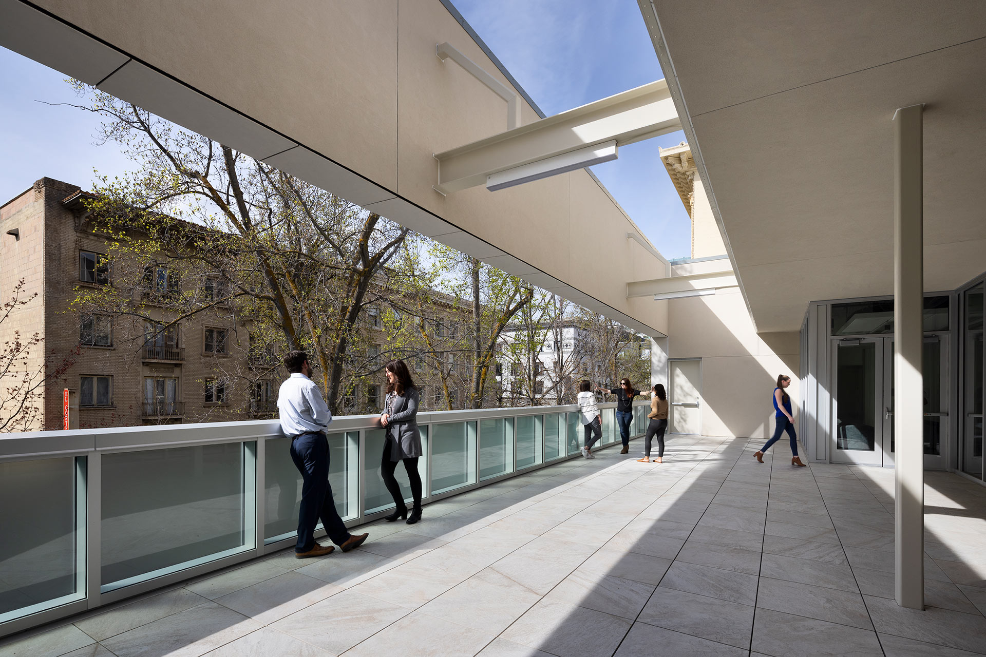 Exterior at UC Center Sacramento academic facility, multiple groups of people gather on an upper level outdoor space with views of the city beyond