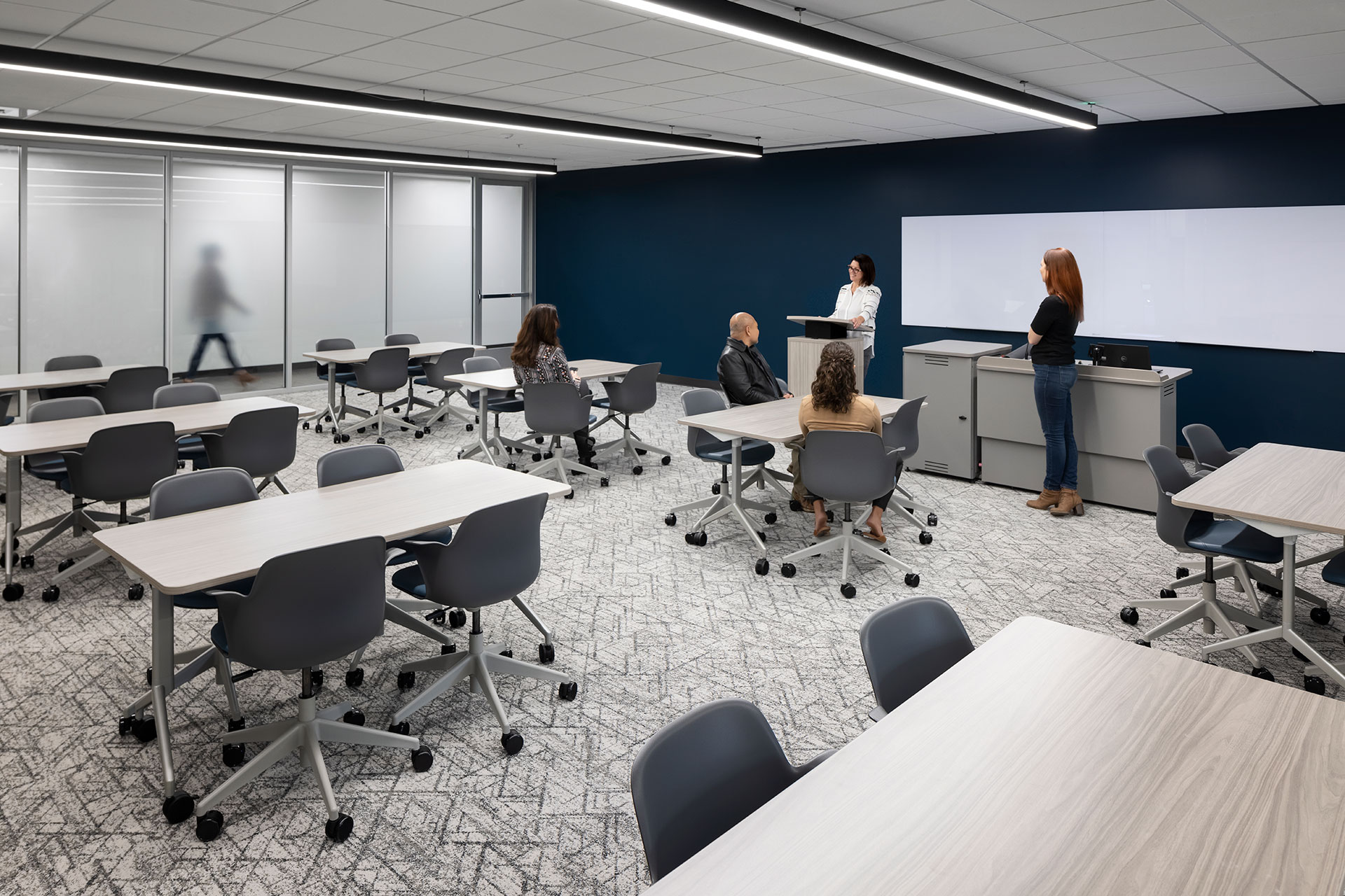 Interior at UC Center Sacramento academic facility, collaboration presentation training room with people sitting at tables and someone standing at a podium at the front