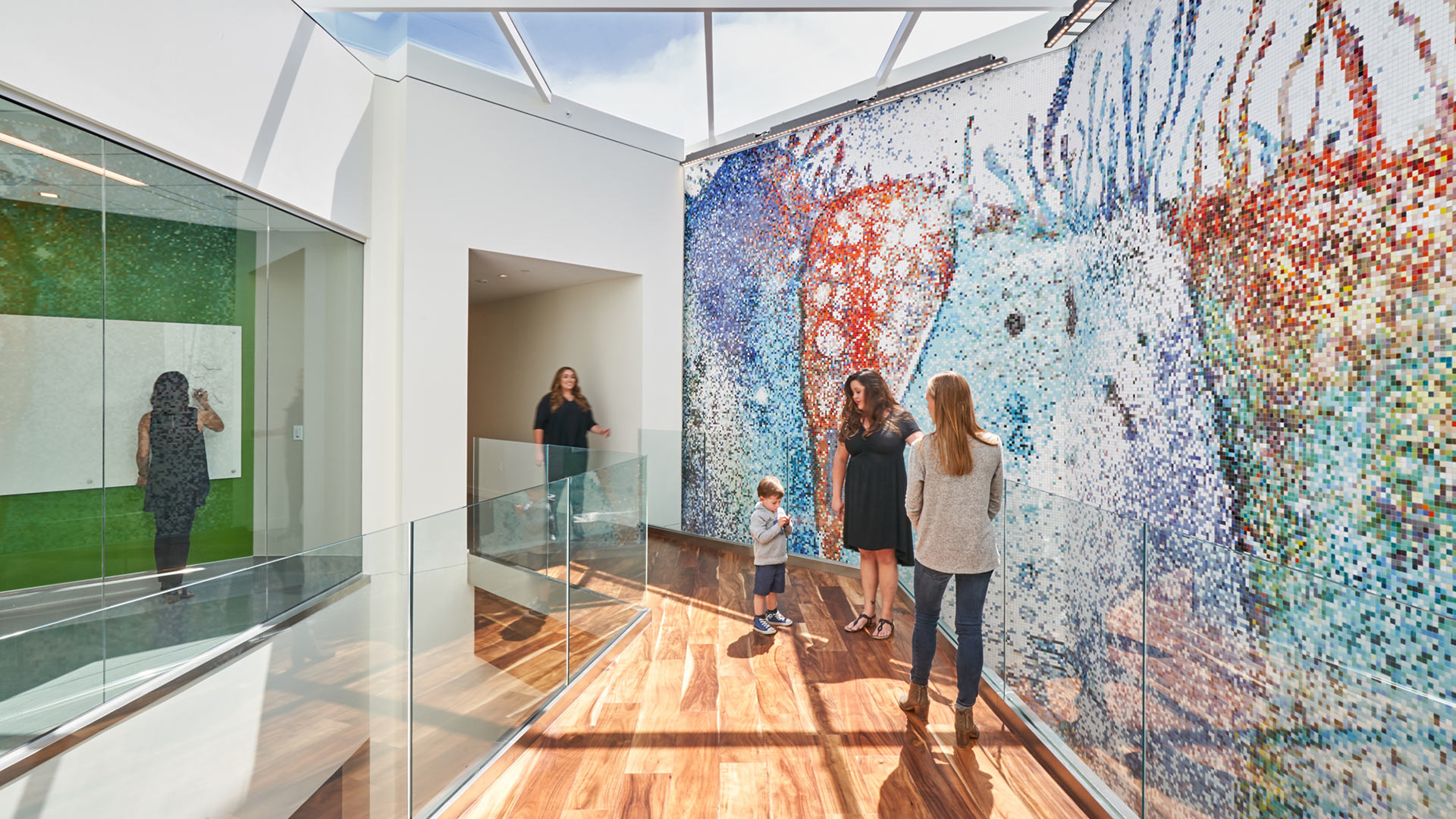 Interior at Vertex Pharmaceuticals life science facility, circulation with large skylight, mosaic art wall feature, and people within the space